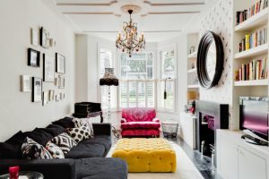 Contemporary living room with white walls and black sofa, a standard fireplace, wall artworks chandelier lamp red accent sofa yellow velvet upholstery table standing lamp floating cabinets