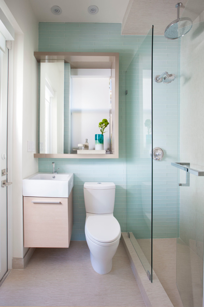 small bathroom with pale blue tiles wall, beige flooring, white toilet, wooden cabinet with white sink on top, mirror