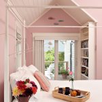 70s Bedroom Pink Walls Pink Vaulted Ceiling White Bed White Side Table Rattan Tray Purple Flower Pot White Shelves Glass Doors
