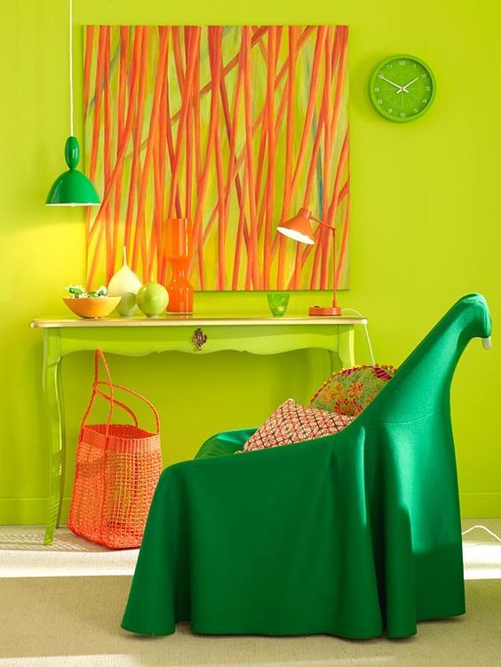 living room with neon yellow wall and table with white marble top, orange painting, orange lamp, orang basket bag, dark green chair, green hanging lamp