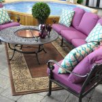 Patio With Concrete Flooring, Brown Rug, Metal Chairs With Purple Cushions, White Blue Pillows, Metal Coffee Table