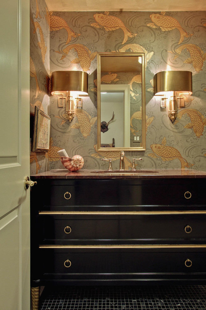 powder room with golden fish patterned wallpaper, dark wood glossy finished cabinet with marble top, golden metallic framed mirror, golden metallic wall lamp