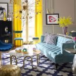 Living Room With Blue Sofa, Blue Chair, Blue Rug, Glass Top Coffee Table, Gold Ottoman, Yellow Curtain