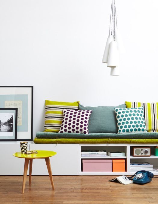 white bench with colourful cushions and pillows, shelves below