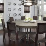 Round Wood Table Top Chandelier Wooden Dining Chairs Wooden Floor Patterned Cushions Wallarts White Walls Glass Windows Rattan Shades French Glass Doors