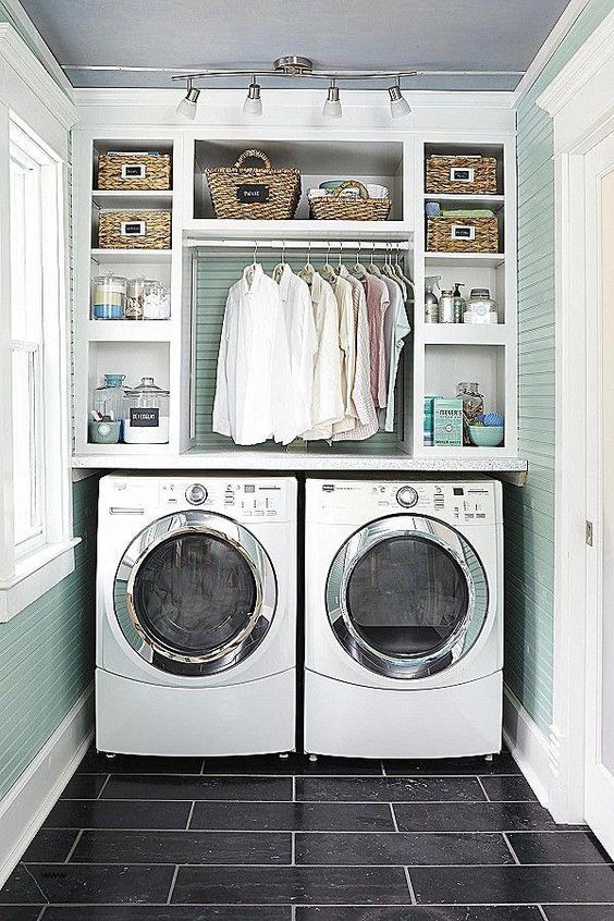small laundry room with green wooden wall, two machines, shelves on top for cleansing liquid, detergent, baskets, and clean clother