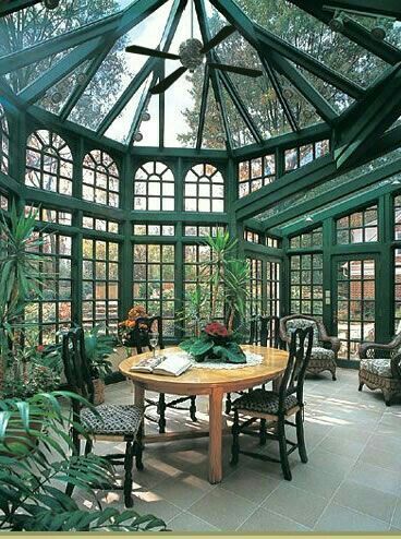 sunroom with green painted framed of windows, ceiling, plants, round dining table and chairs, ceiling fan
