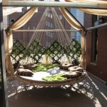 Swing Hammock Bed White Rope Round Hammock Bed Wooden Flooring Open Space Red Brick Walls Black Glass Window Green Throw Brown Pillows Cream Drapes
