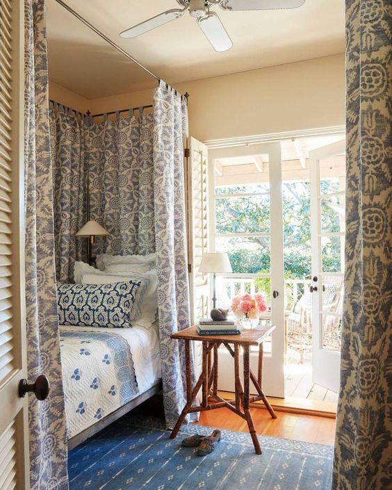 bed nook, wooden floor, blue rug, blue white bedding, blue pattern curtain on rail, white wall, glass door