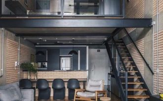 two levels apartment, wooden floor, bedroom on the upper evel with glass rail, living room with grey sofa, kitchen with open brick island and black chairs at the bottom
