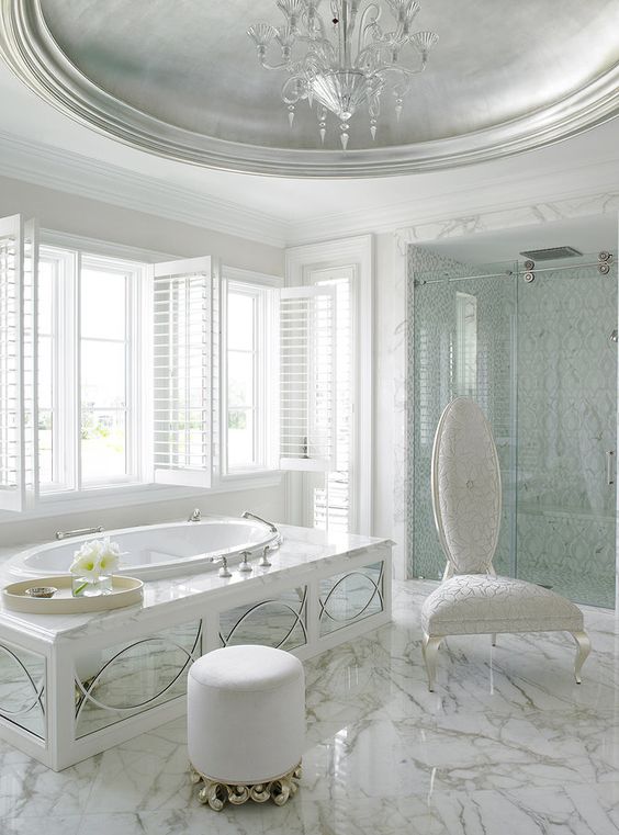 bathroom, white marble floor, white wall, white marble tub, white chair, white ottoman, white ceiling, silver round indented ceiling, chandelier, shower room