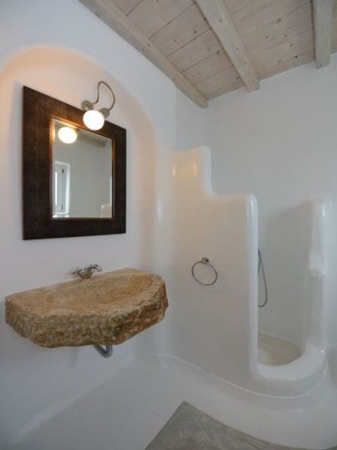 greek bathroom, white plaster wall and floor, floating stone sink, mirror, indented wall, wooden ceiling, grey rug