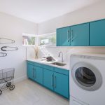 Laundry Room Decorations Glass Corner Windows Blue Cabinets White Countertop Big Pins Decorations Sink Faucet White Walls Washing Machine