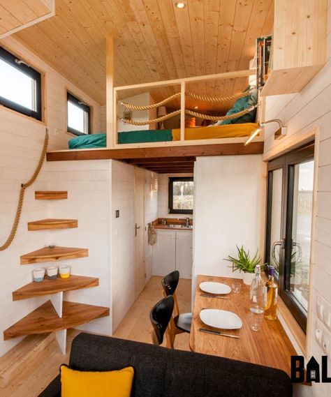 tiny house, wooden floor, wooden wall, kitchen at the back, dining table, black sofa, bed upstairs, corner stairs without rail