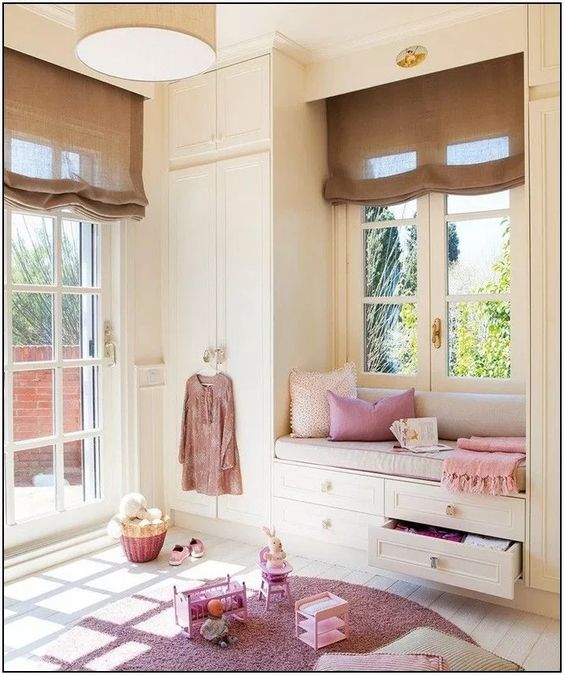 children's bedroom, white window seat with drawers, white wooden floor, pink rug, white cupboard, brown shade, round brown pendant
