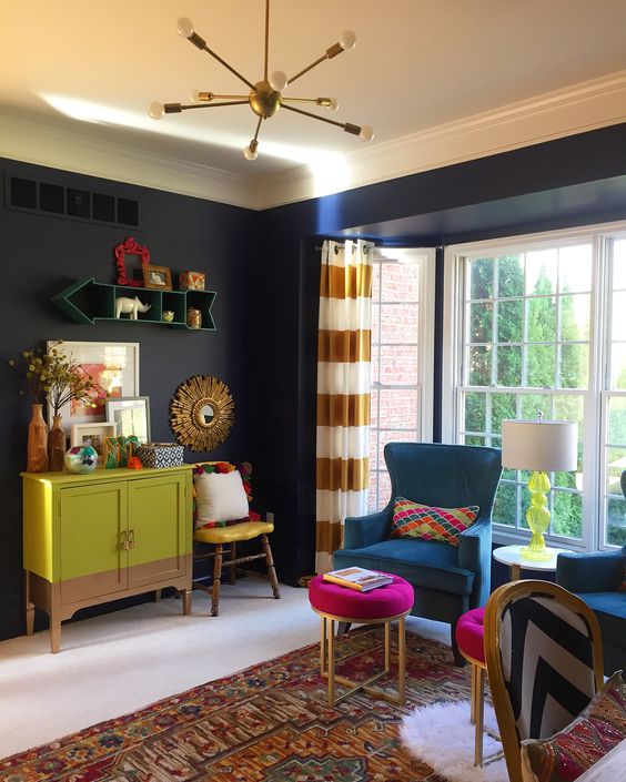 living room, white floor, black wall, patterned rug, blue chairs, pink ottoman, green cabinet, modern pendant